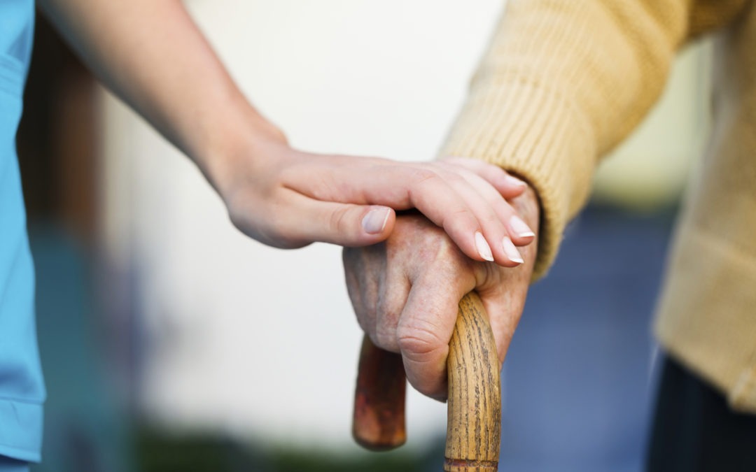 A soft hand touches an elderly hand holding a cane