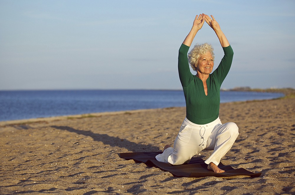 An elderly woman practices yoga at a beach